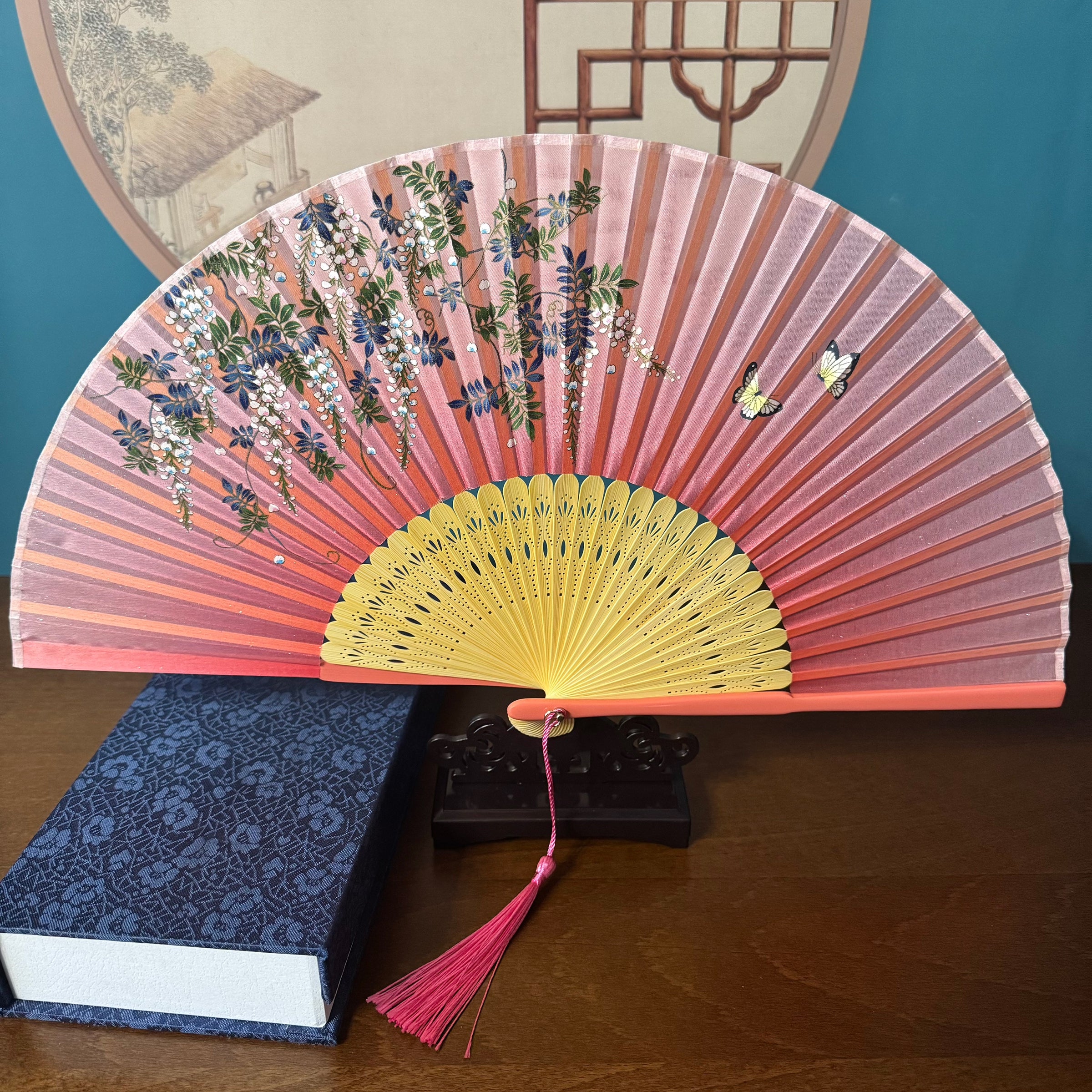 Chinese style Hand held bamboo folding fan on a fan stand with handcrafted box on the side. The background is Chinese ink-wash window paper-cuts.