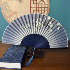 Chinese style Hand held bamboo folding fan on a fan stand with handcrafted box on the side. The background is Chinese ink-wash window paper-cuts.