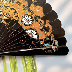 Details of the gold-sprinkled patterns of an East Asian Lacquer Folding Fan (Urushi fan). The background is sunlight, and palm leaves.