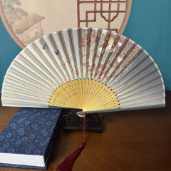 Chinese style hand held bamboo folding fan on a fan stand with handcrafted box on the side. The background is Chinese ink-wash window paper-cuts.