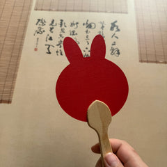 A rabbit shape red fixed fan in front of a Chinese calligraphy
