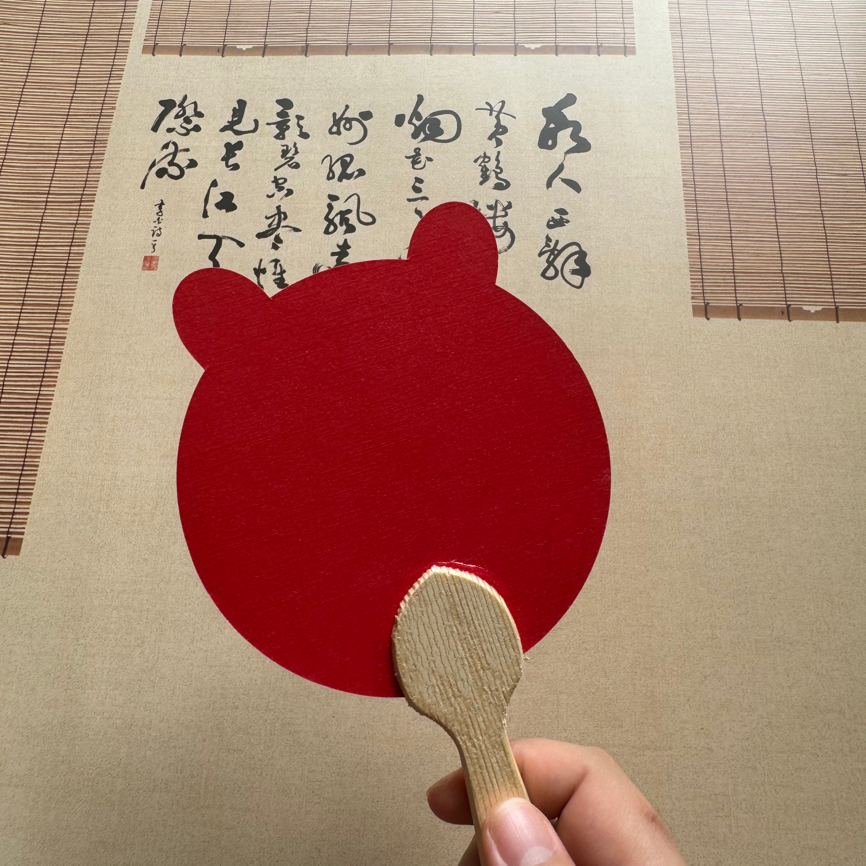 A bear shape red Chinese round fan in front of a Chinese calligraphy