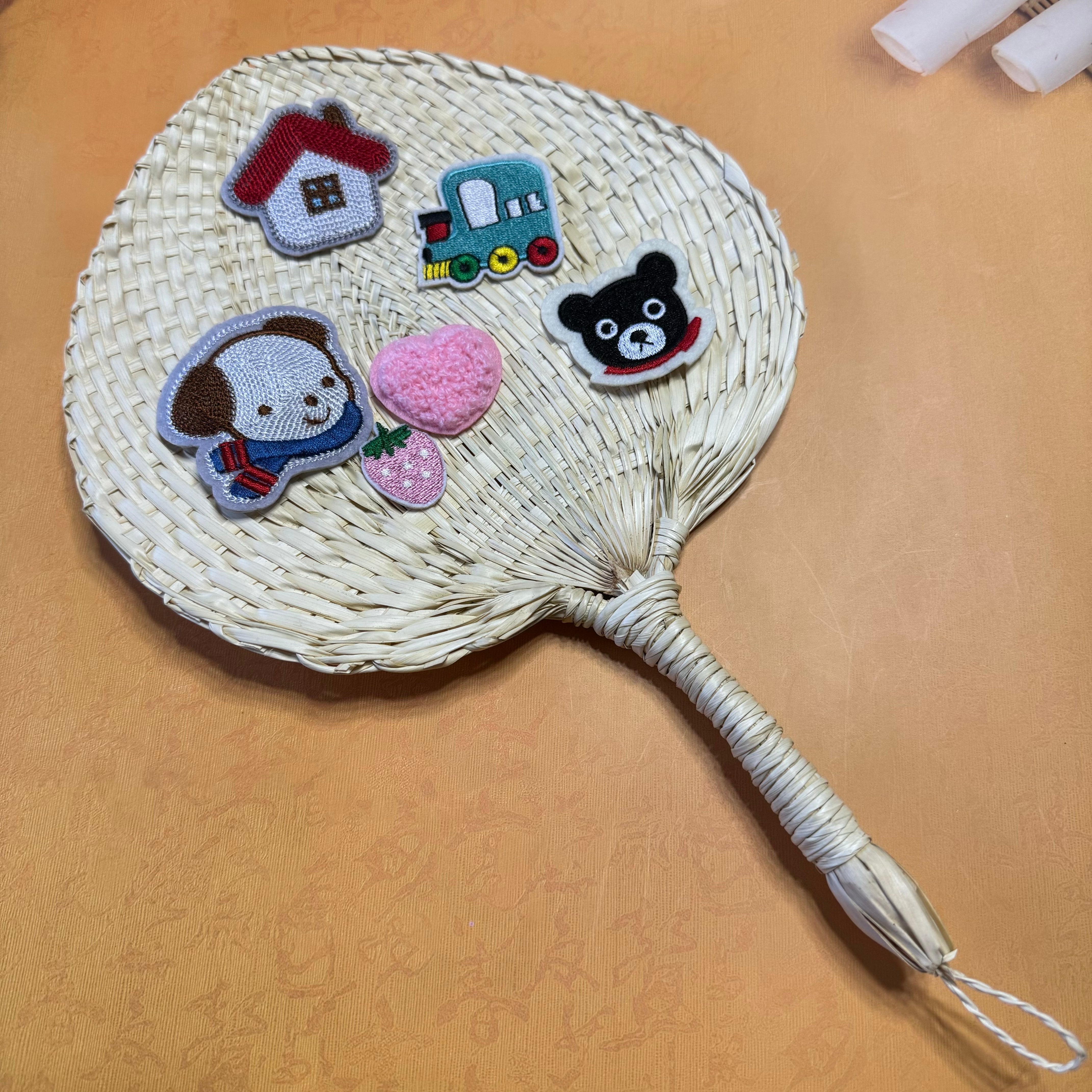 A palm leaf fan on a table, some stickers are on top of the fan