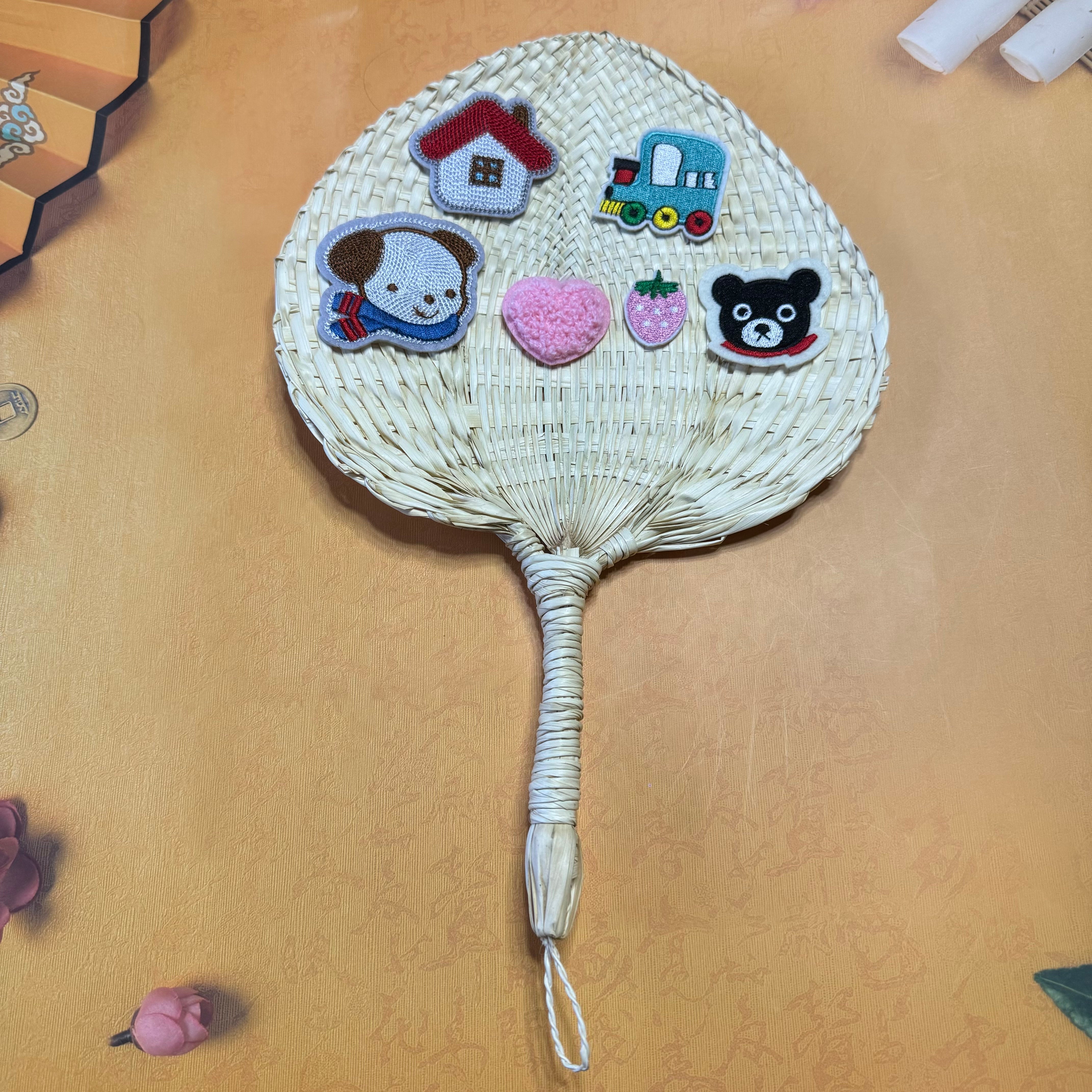 A palm leaf fan on a table, some stickers are on top of the fan