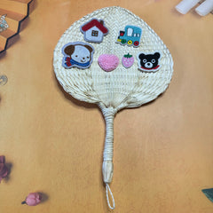 A palm leaf fan on a table, some stickers are on top of the fan