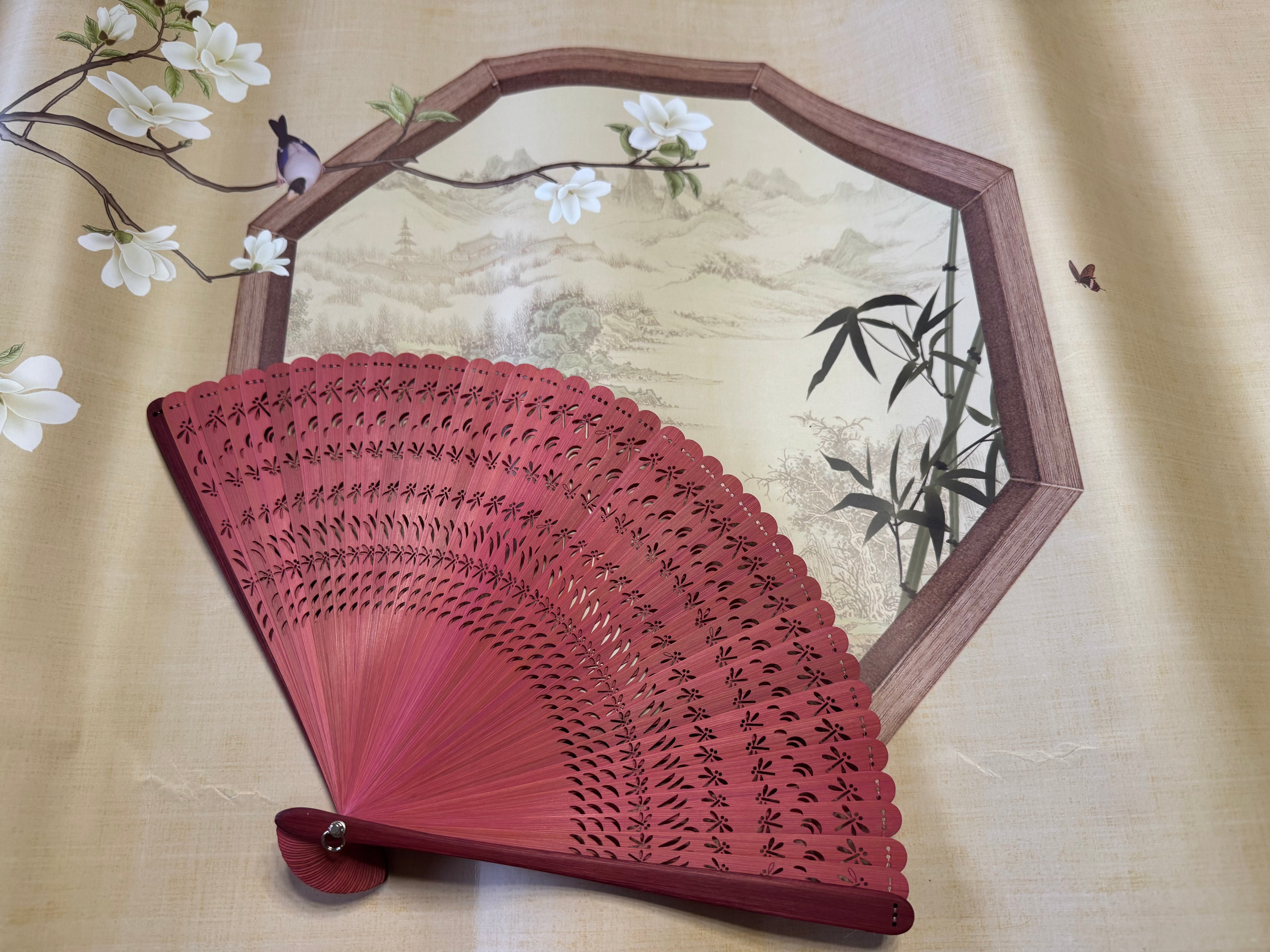 a red touqing bamboo fan on a cloth featuring Chinese artistic motifs