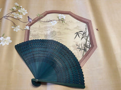 a green touqing bamboo fan on a cloth featuring Chinese artistic motifs