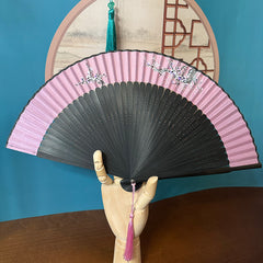 a wooden hand holding a fan in front of a Chinese painting