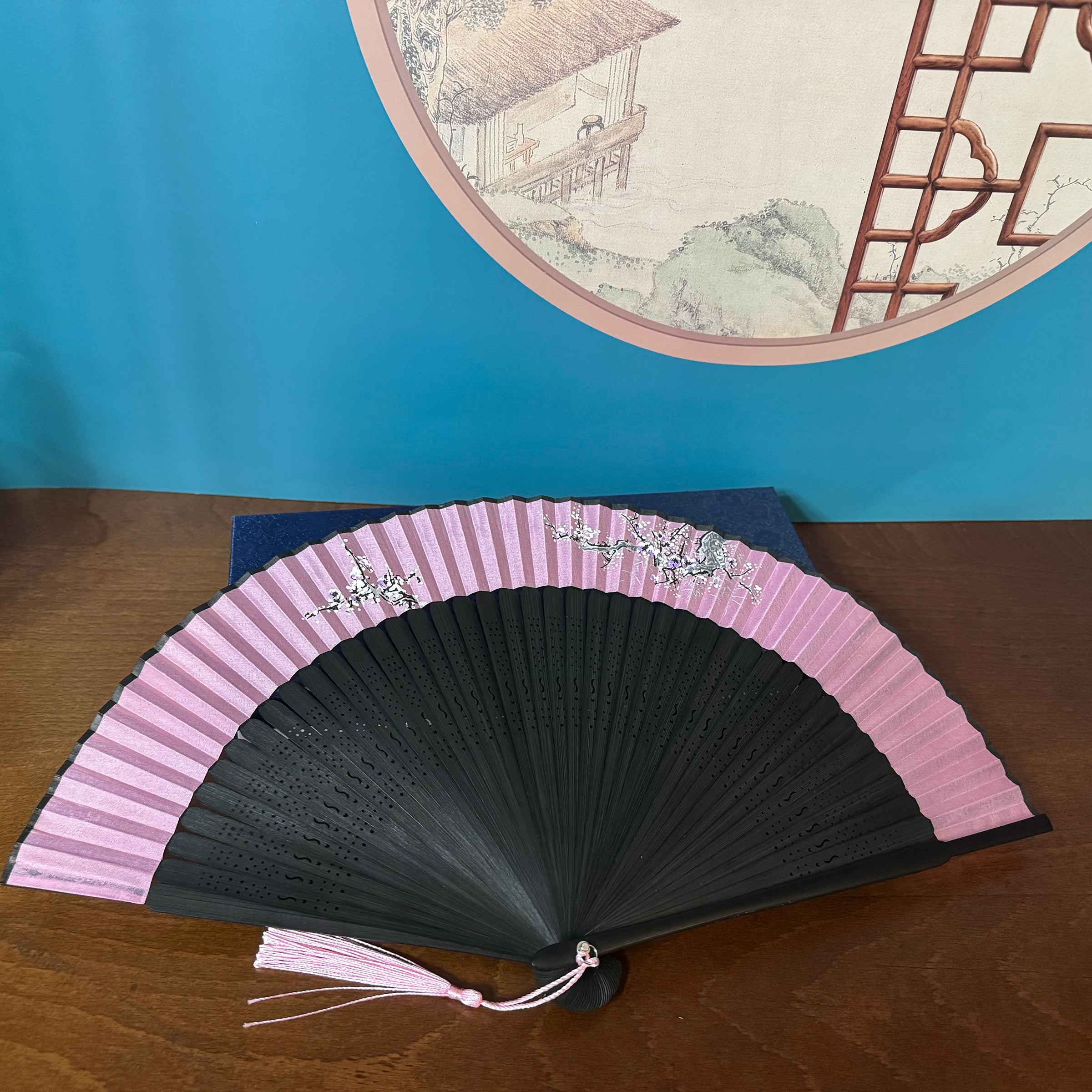 a plum blossom fan is placed on a dark blue box with surface patterns