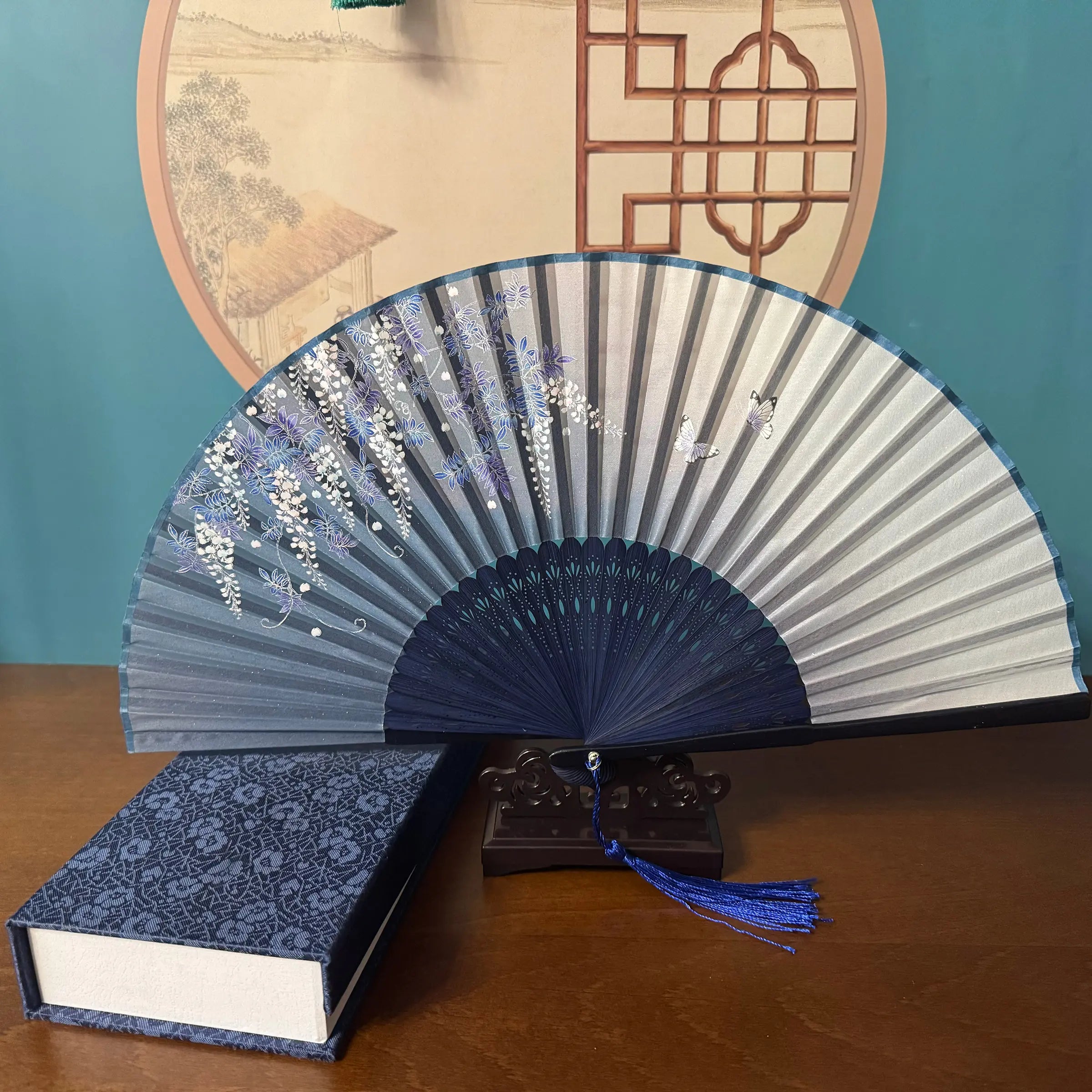 Chinese style hand held bamboo folding fan on a fan stand with handcrafted box on the side. The background is Chinese ink-wash window paper-cuts.