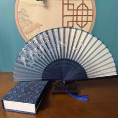 Chinese style hand held bamboo folding fan on a fan stand with handcrafted box on the side. The background is Chinese ink-wash window paper-cuts.