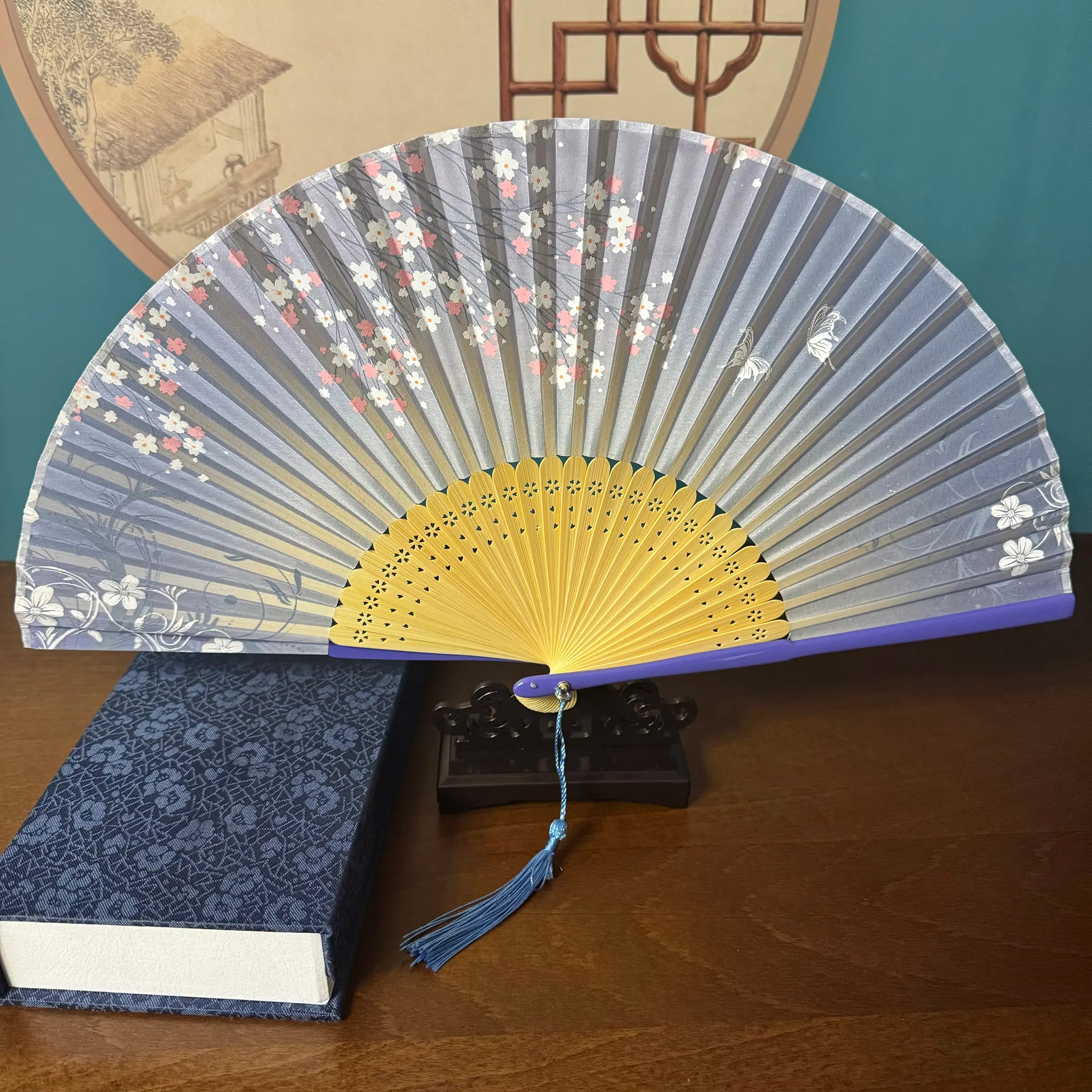 Chinese style hand held bamboo folding fan on a fan stand with handcrafted box on the side. The background is Chinese ink-wash window paper-cuts.