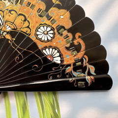 Details of the gold-sprinkled patterns of an East Asian Lacquer Folding Fan (Urushi fan). The background is sunlight, and palm leaves.