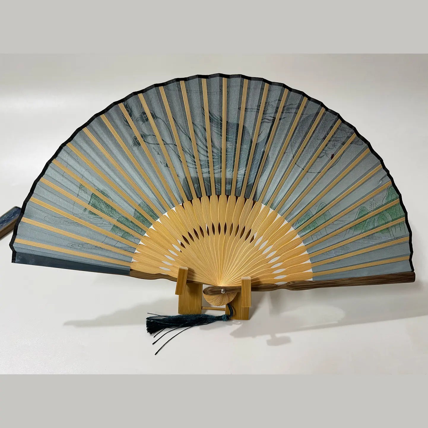 The back side of a Chinese silk phoenix folding fan is displayed on a fan stand.