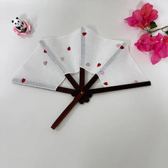 A elegant classical hand fans with delicate little red heart embroidery, displayed on a white surface. There are pink flowers and a cute panda figurine in the background.