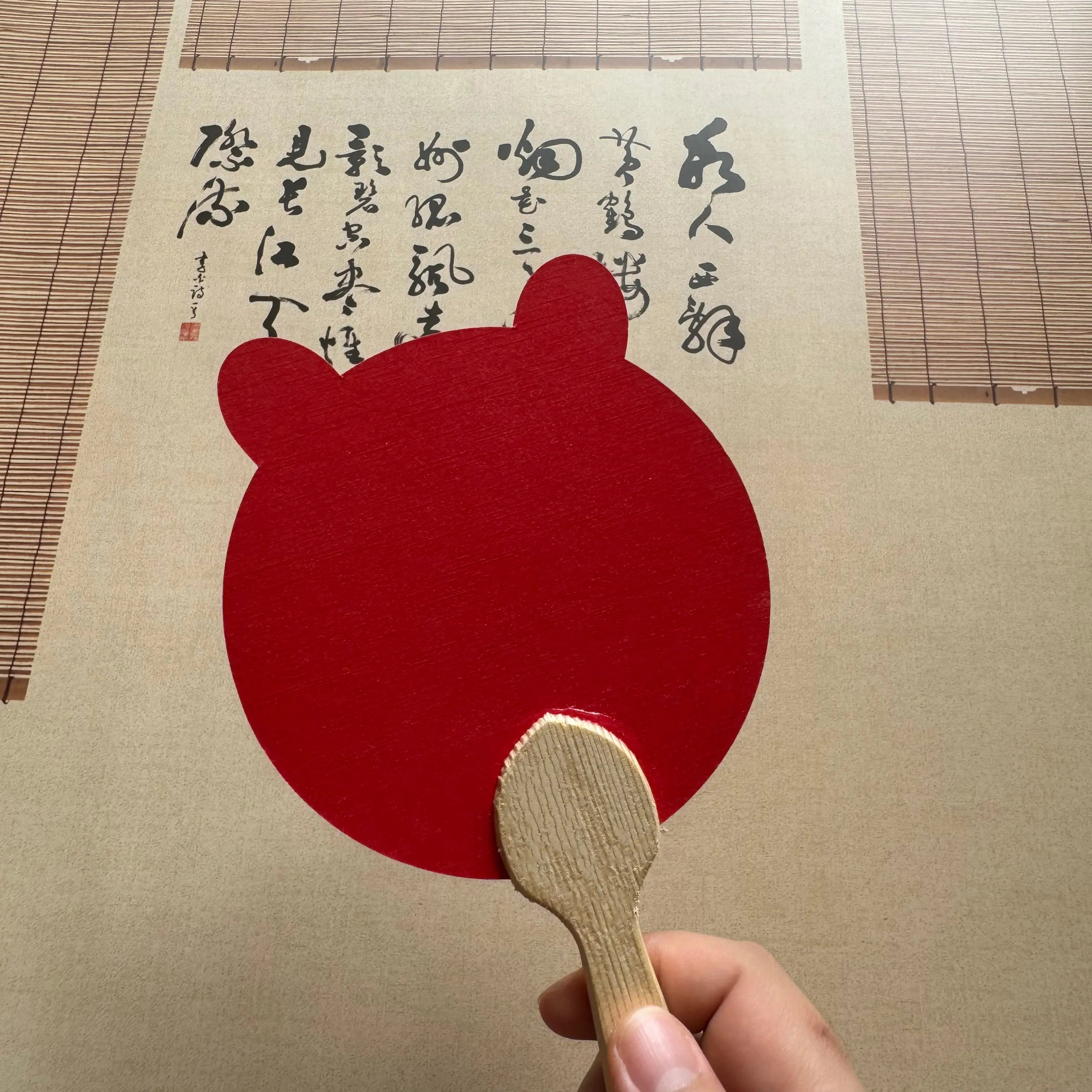 A bear shape red Chinese round fan in front of a Chinese calligraphy