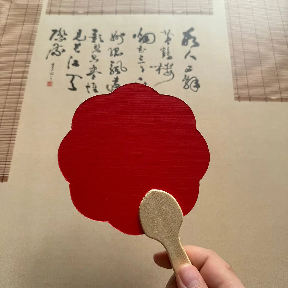 A eight-petal flower shape red fixed fan in front of a Chinese calligraphy