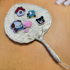 A palm leaf fan on a table, some stickers are on top of the fan