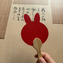 A rabbit shape red fixed fan in front of a Chinese calligraphy