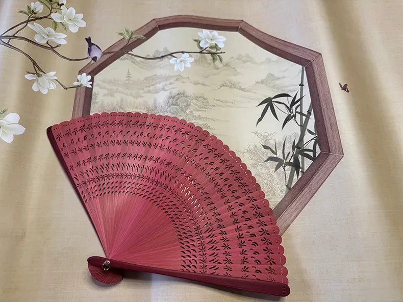 a red touqing bamboo fan on a cloth featuring Chinese artistic motifs