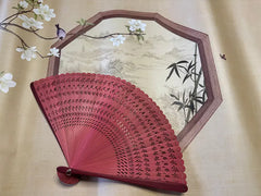 a red touqing bamboo fan on a cloth featuring Chinese artistic motifs
