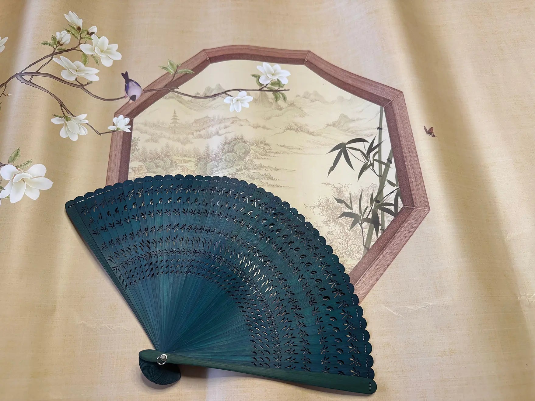 a green touqing bamboo fan on a cloth featuring Chinese artistic motifs