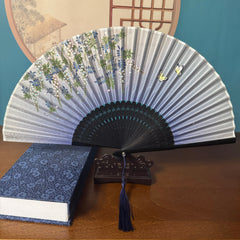 Chinese style Hand held bamboo folding fan on a fan stand with handcrafted box on the side. The background is Chinese ink-wash window paper-cuts.
