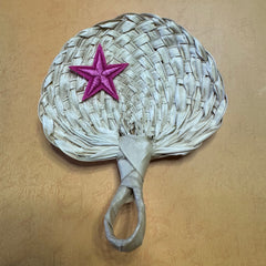 A hand size palm leaf fan on a table, a star shape sticker is on top of the fan