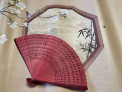 a red touqing bamboo fan on a cloth featuring Chinese artistic motifs