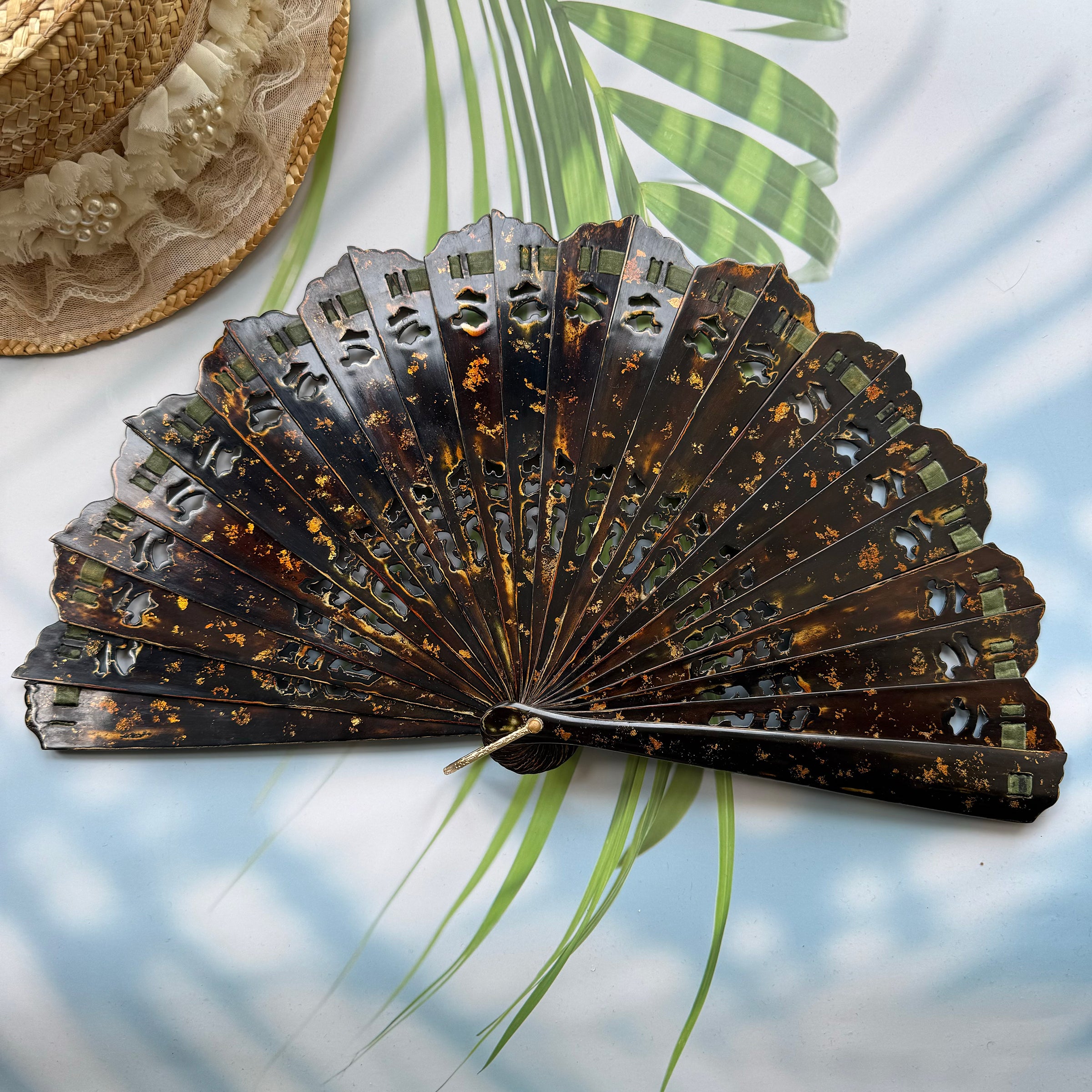 On the table lies an East Asian Lacquer Folding Fan (Urushi fan) with a hollowed-out rib design and gold-sprinkled patterns. 