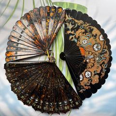 3 Chinese lacquer folding fan with gold-sprinkled patterns are placed on a table.