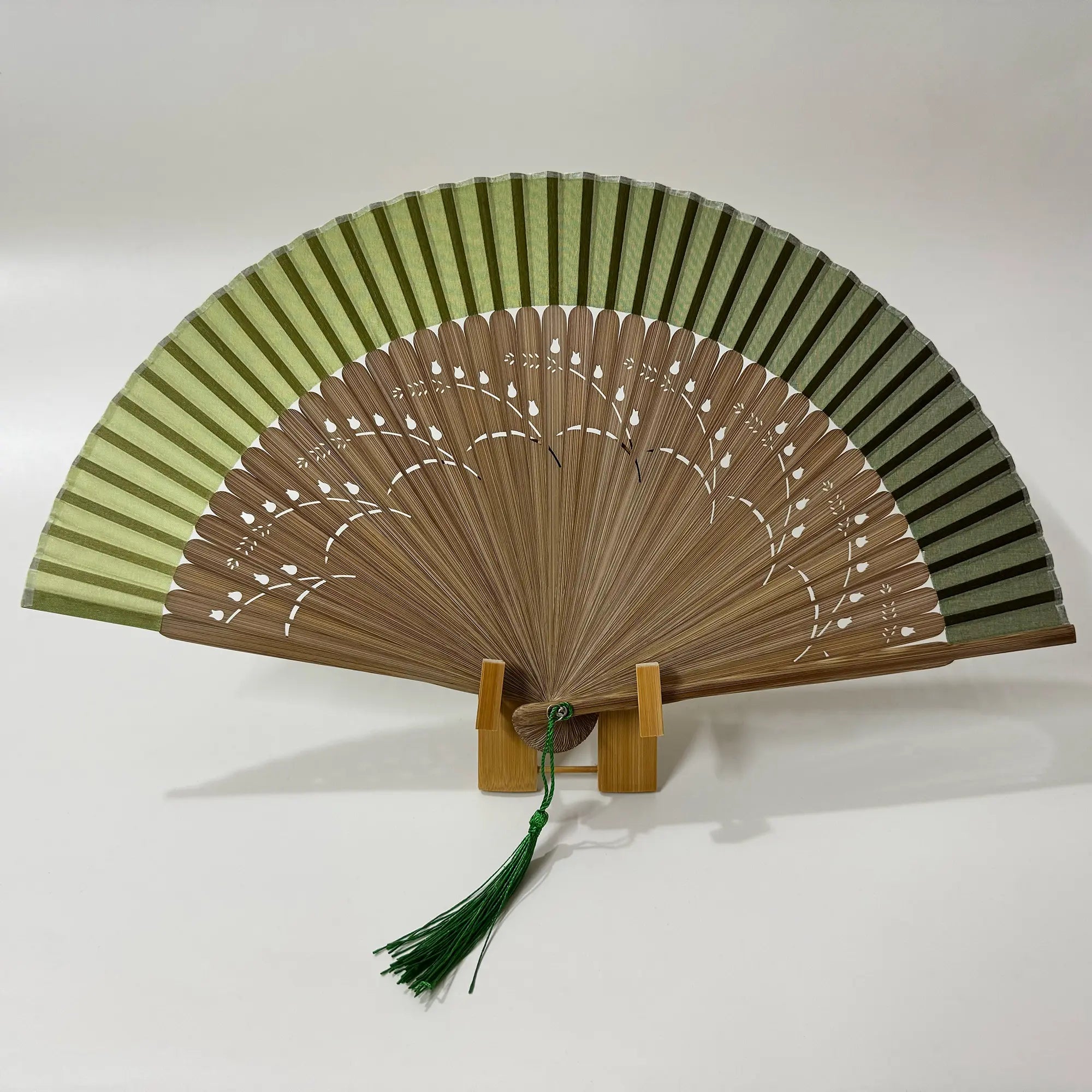 A pomegranate flower carved bamboo folding fan with green tassel. Gradient green fan panel.