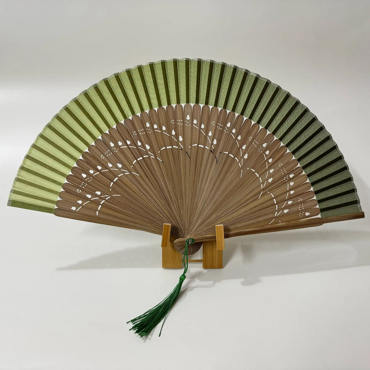 A pomegranate flower carved bamboo folding fan with green tassel. Gradient green fan panel.
