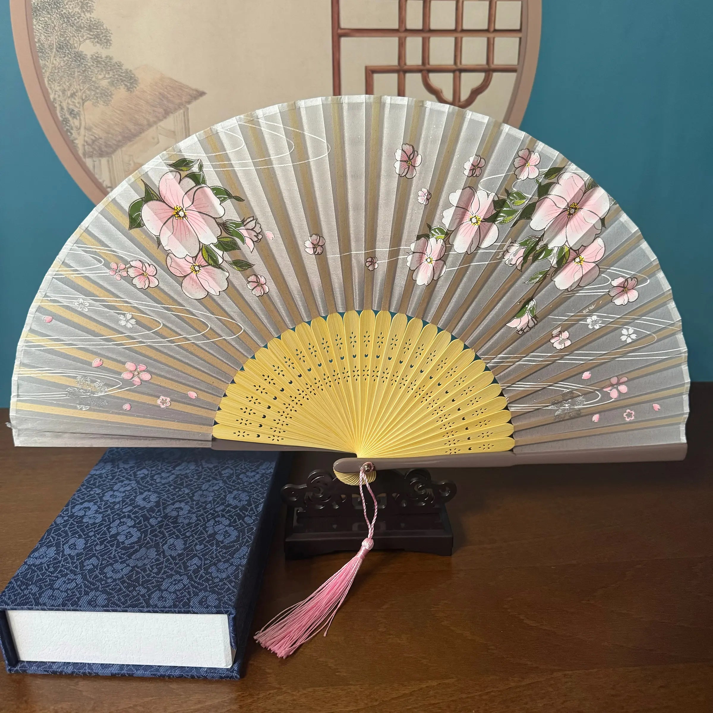Chinese style hand held bamboo folding fan on a fan stand with handcrafted box on the side. The background is Chinese ink-wash window paper-cuts.