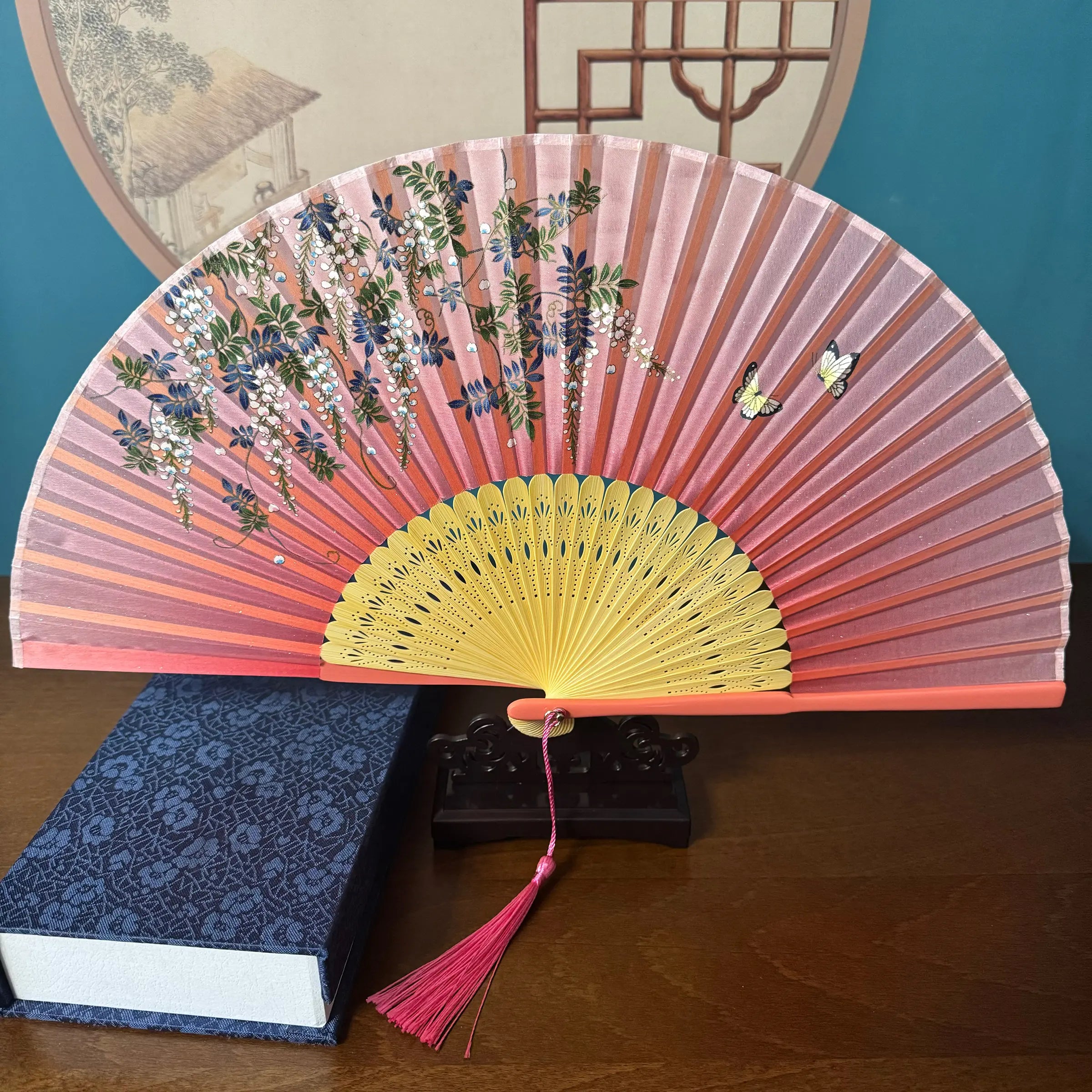 Chinese style hand held bamboo folding fan on a fan stand with handcrafted box on the side. The background is Chinese ink-wash window paper-cuts.
