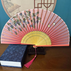 Chinese style hand held bamboo folding fan on a fan stand with handcrafted box on the side. The background is Chinese ink-wash window paper-cuts.