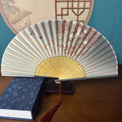 Chinese style hand held bamboo folding fan on a fan stand with handcrafted box on the side. The background is Chinese ink-wash window paper-cuts.