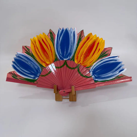 Decorative hand-painted Spanish fan featuring a cheerful yellow and blue tulips drawing. Styled shot on a white surface with a fan stand.