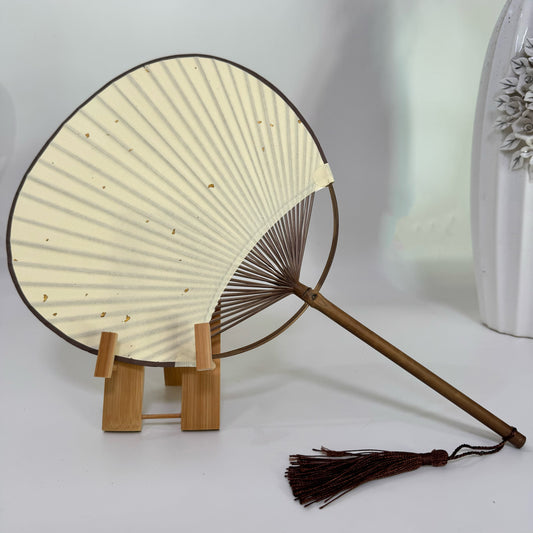 A Japanese round fan is placed on a fan stand. The fan is made of blank gold-sprinkled Chinese art paper, with a white background and a white vase.