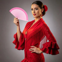 A Spanish fan in pink color is held by a dancer in traditional Spanish red dress. A performance prop and decorative handcraft.