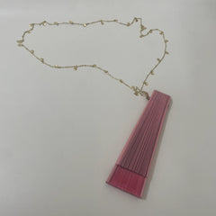 A folded Spanish-style fan in pink with a gold charm on its handle, resting on a white surface.