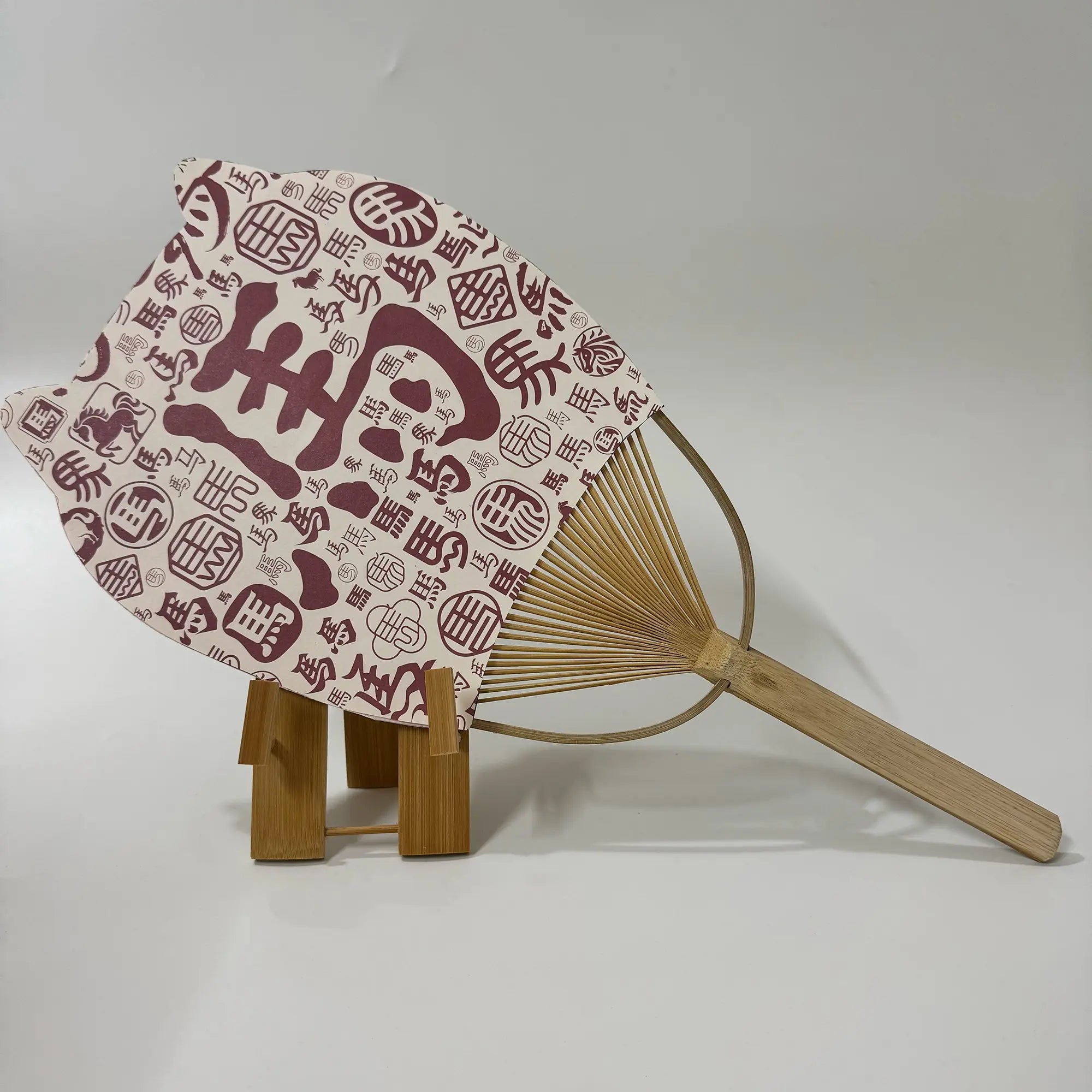 A Japanese round fan (uchiwa fan) with cat ears. On the fan panel it prints Chinese characters says horse. 