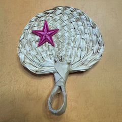 A hand size palm leaf fan on a table, a star shape sticker is on top of the fan
