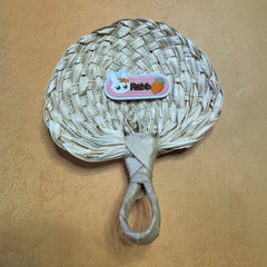 A hand size palm leaf fan on a table, a small rabbit sticker is on top of the fan