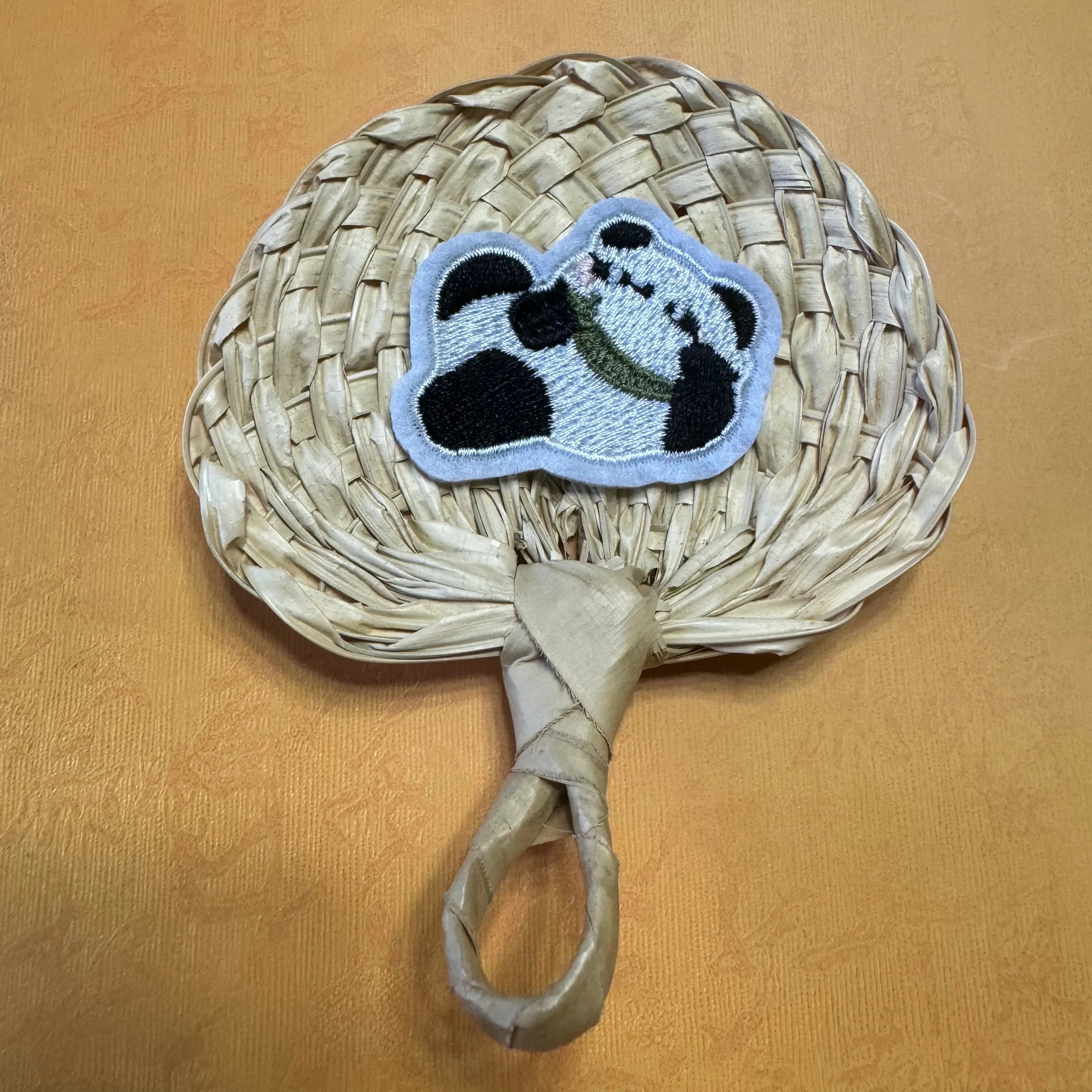A hand size palm leaf fan on a table, a panda shape sticker is on top of the fan